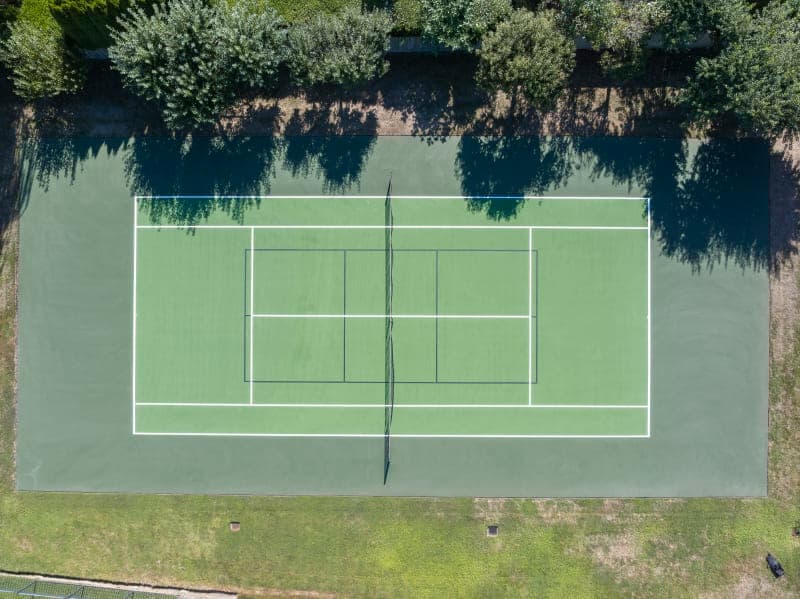 Aerial drone shot of completed residential tennis court resurfacing with custom blue and green color design
