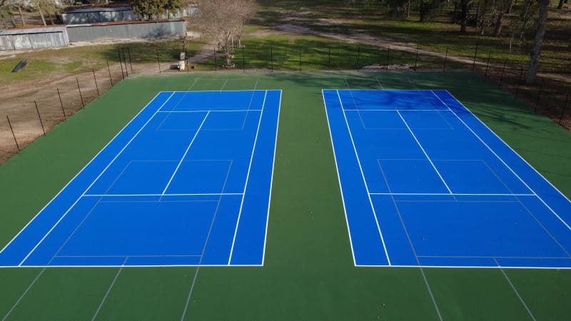 Aerial view of two resurfaced tennis courts with blue and green acrylic surface at Yoakum City Park in Texas