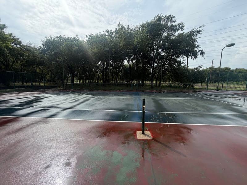 Before photo of a weathered red and blue tennis court with faded surface before resurfacing in Richardson, Texas