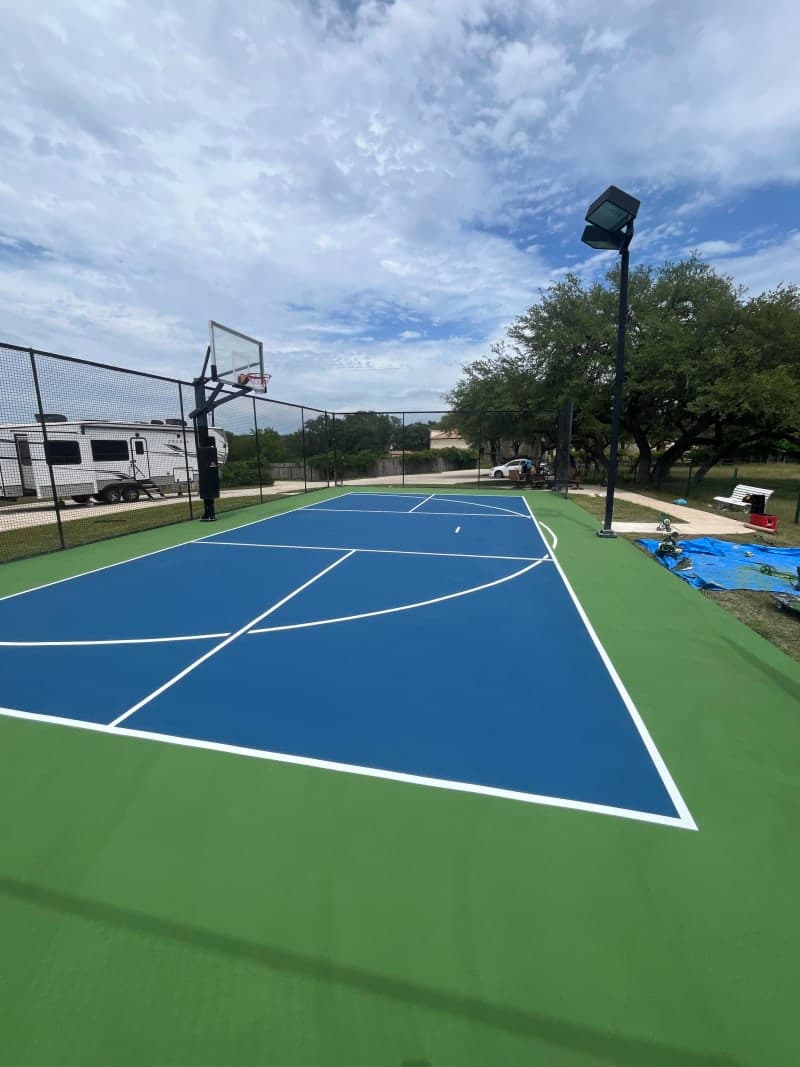 After photo of a freshly resurfaced blue and green multi-sport basketball court with crisp white lines in Wimberley, Texas